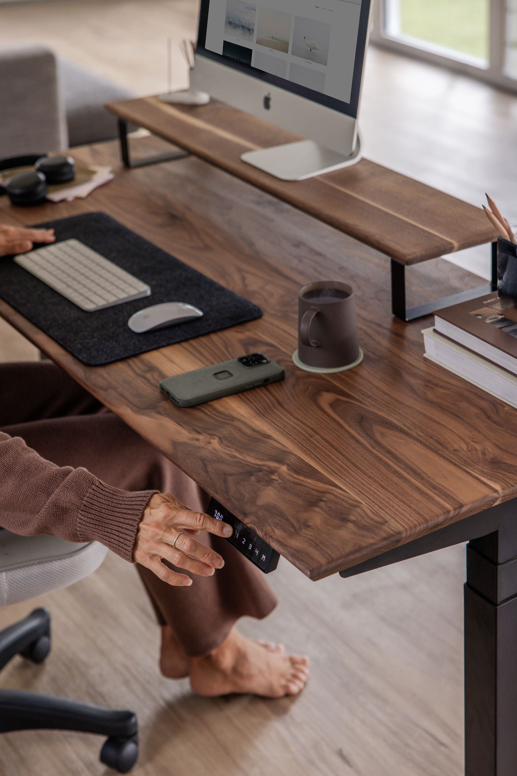 Detail shot of Upwood standing desk's digital height control panel, featuring rich American walnut desktop surface and modern office accessories