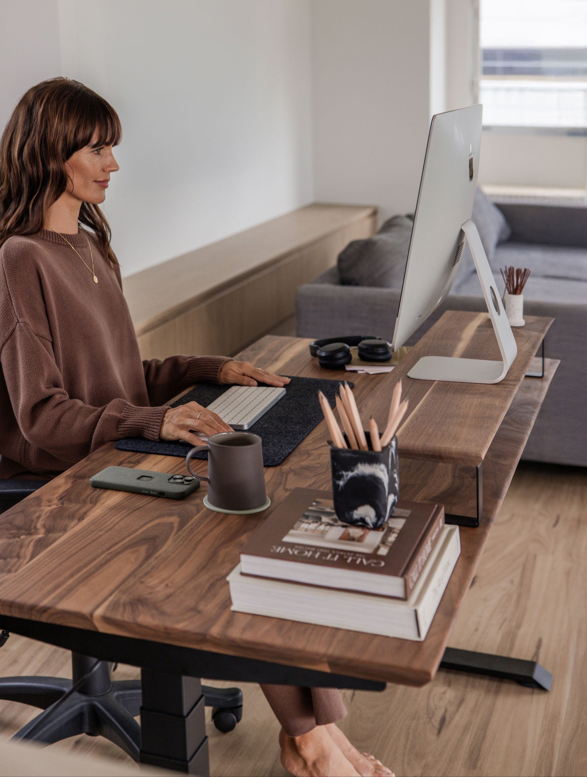 Upwood monitor riser in American walnut elevating iMac to ergonomic height, styled with matching standing desk, keyboard mat, and minimalist desk accessories for optimal workspace organization